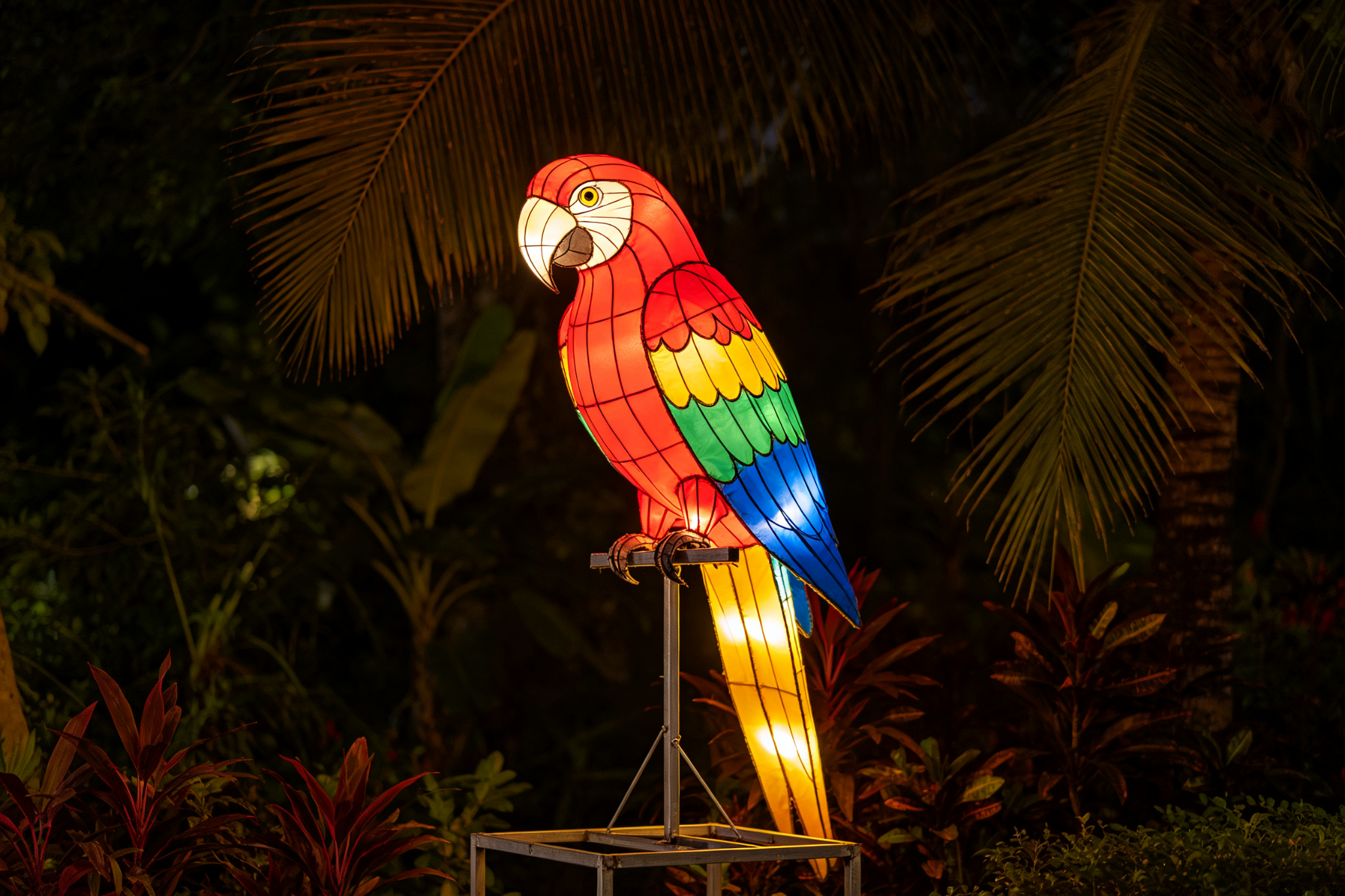 Colorful red parrot lantern on stand among tropical plants